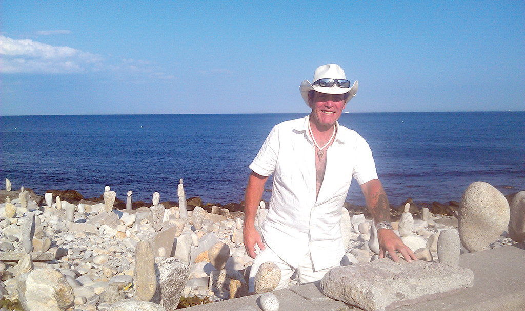ROCK STAR: Joseph DiPietro, known to his friends and family as “J.D. Mystery,” enjoys creating rock art at local beaches, as well as remodeling homes with recycled products. Here, he smiles with his rock art at Narragansett Beach.
