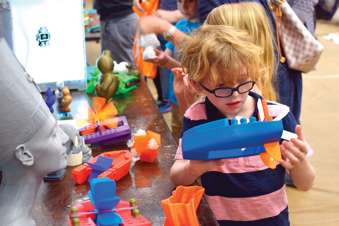 NEVER TOO YOUNG TO APPRECIATE A WELL-DESIGNED BOAT: A spectator at the Robot Block Party explores 3D Printed paddleboats created by members of the Ocean State Maker Mill.