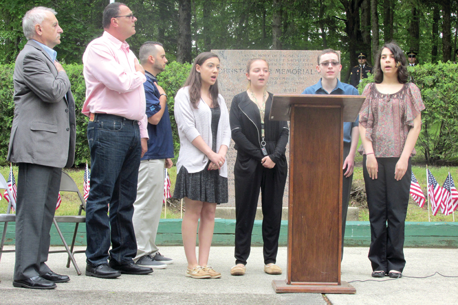 MEMORIAL MOMENT: Johnston Mayor Joseph Polisena (left), Parks & Recreation Director Dan Mazzulla and emcee Mike Bedrosian stand at attention as Johnston High chorus members Isabella Parrillo, Madison Paolucci, Matthew Eisemann and Kathleen Jaroma sing the national anthem during Saturday’s annual Memorial Day service.