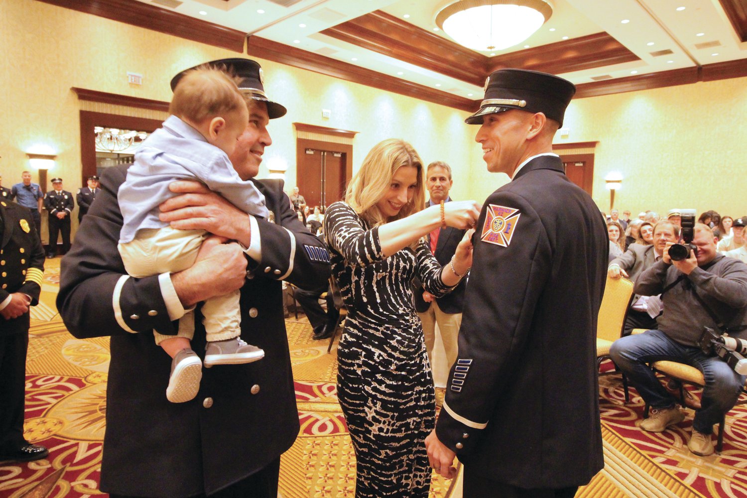 WHAT IT TAKES TO BE PINNED: Lt. Michael Boynton Jr., who served as master of ceremonies, is pinned by his wife, Deonna. Looking on is his father, Warwick Fire Lt. Michael Boynton Sr., who is holding his grandson, Calvin.