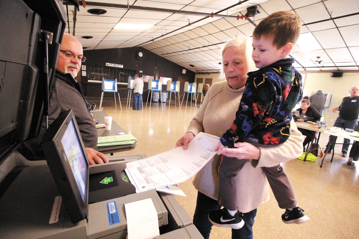 LESSON IN VOTING: Carol Palumbo accompanied by her 4-year-old grandson, Oliver Kennedy, was among the first 100 voters to cast ballots at the William Shield Post poll in Conimicut. Oliver got to feed his grandmother’s ballot into the machine and an “I voted” sticker