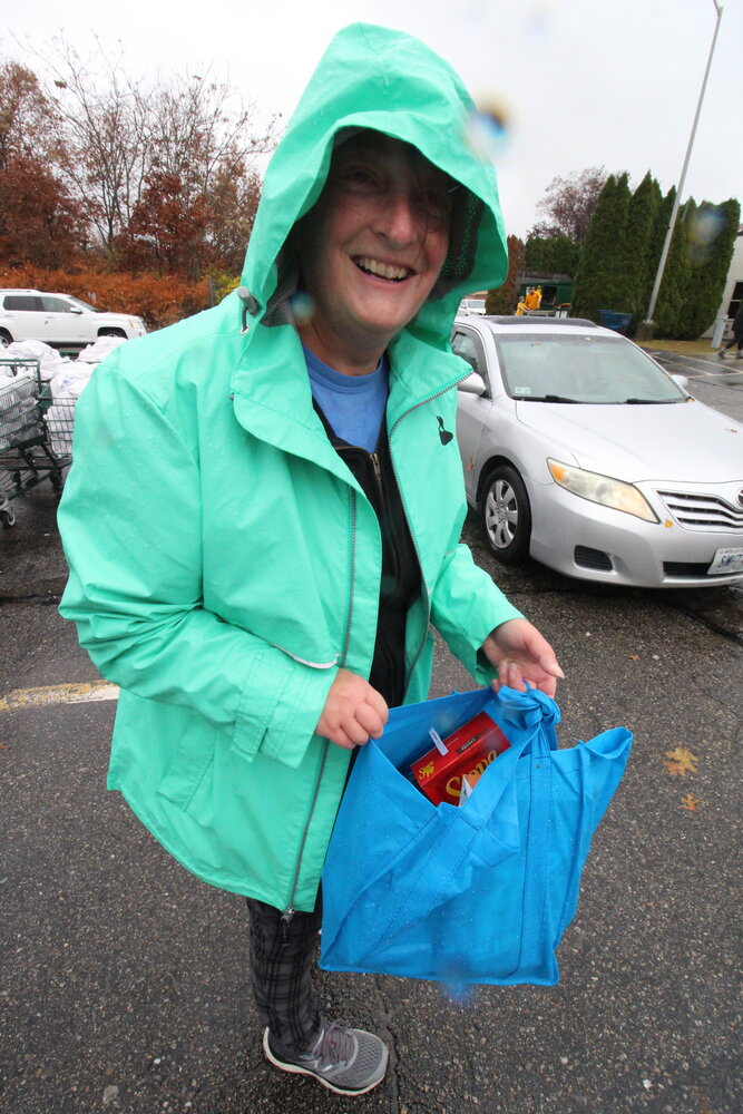 BUT SHE DIDN’T HAVE BOOTS: Appropriately, Carol Berry wore a rain jacket as she handed out bags (courtesy of Blue Cross) with canned food at the Westbay Community Action pickup Saturday morning. She regretted not wearing boots.